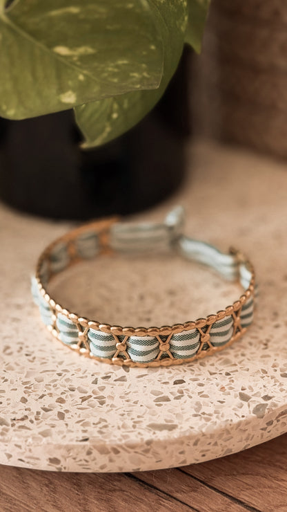Bracelet jonc en acier inoxydable et tissu upcyclé motif rayé bleu et blanc, posé sur un plateau en terrazzo