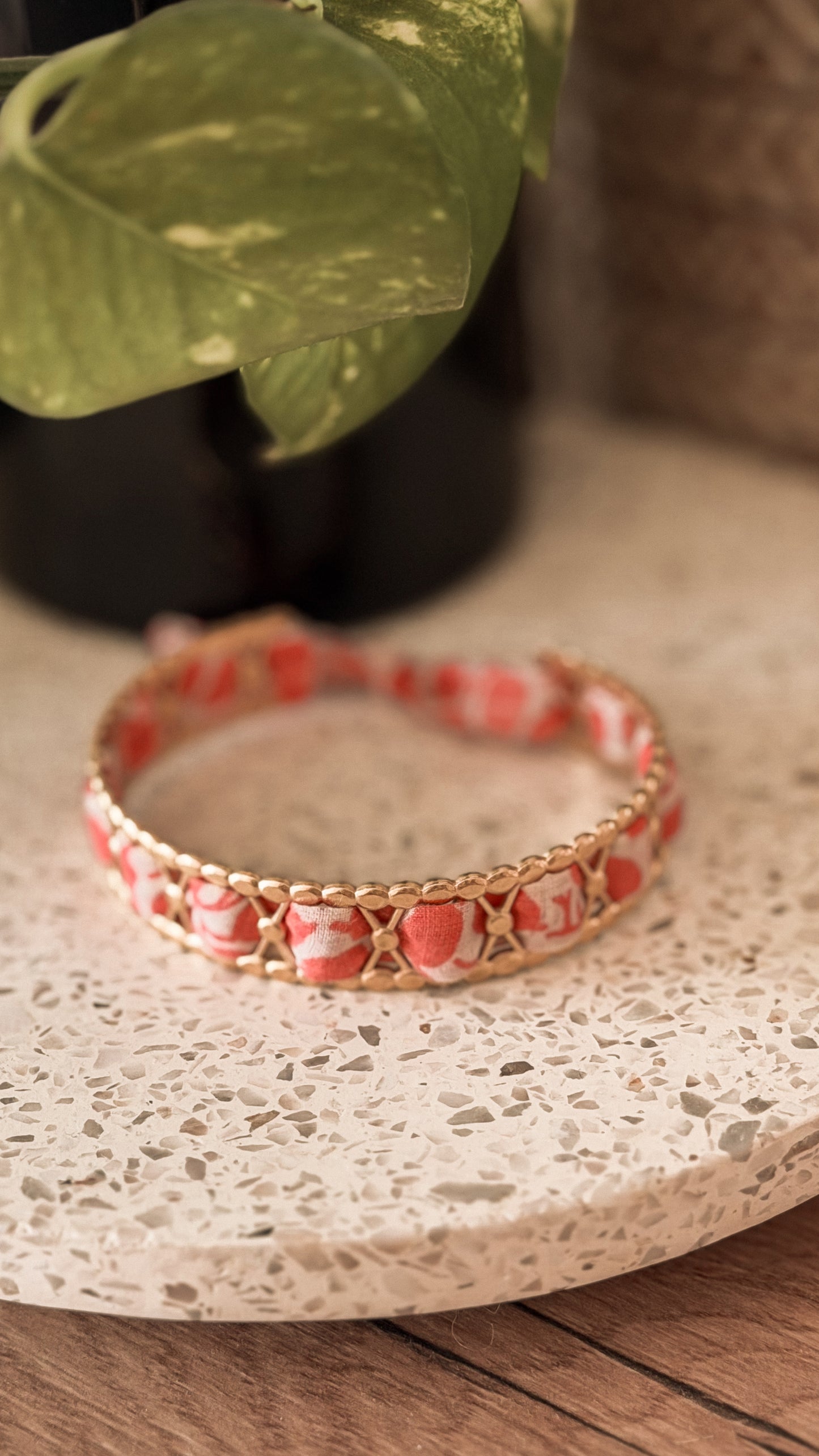 Bracelet jonc en acier inoxydable et tissu upcyclé motif rose corail, posé sur un plateau en terrazzo