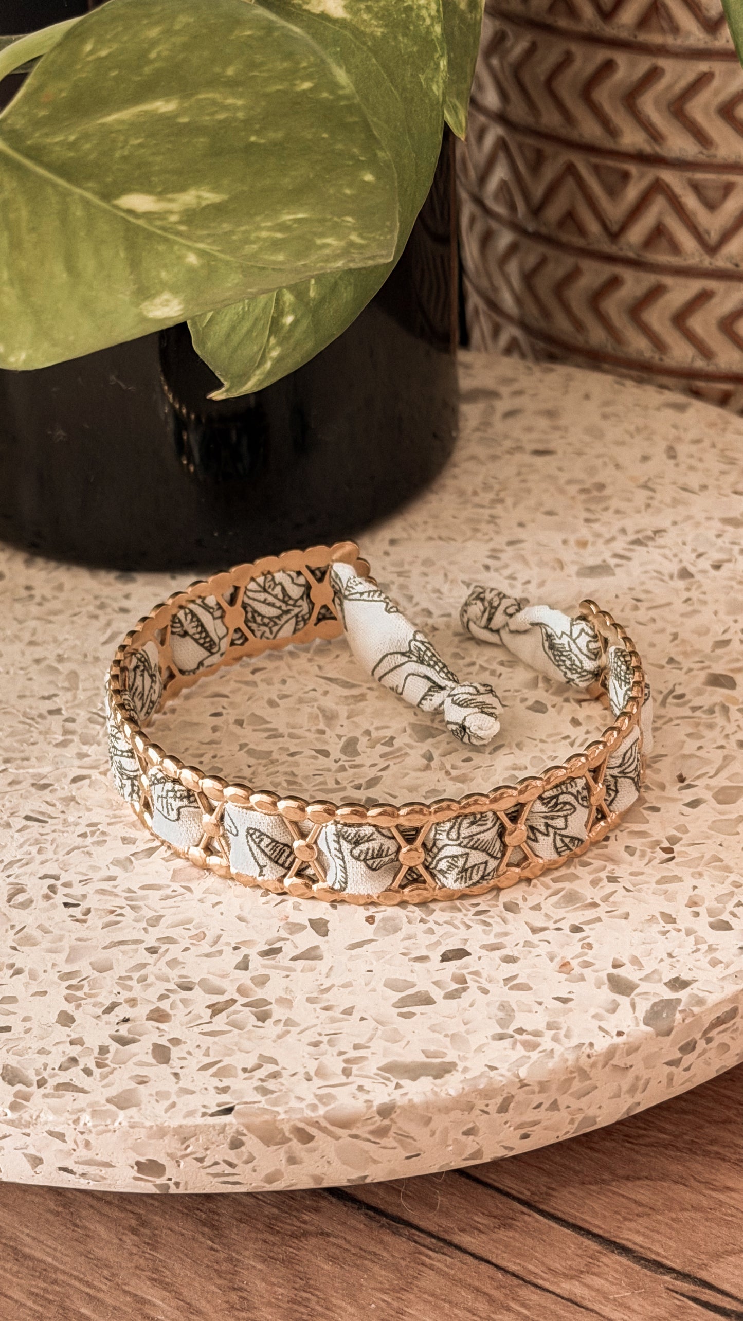 Bracelet jonc en acier inoxydable et tissu upcyclé motif feuilles noir et blanc, posé sur un plateau en terrazzo