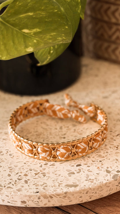 Bracelet jonc en acier inoxydable et tissu upcyclé motif feuilles ocre et blanc, posé sur un plateau en terrazzo