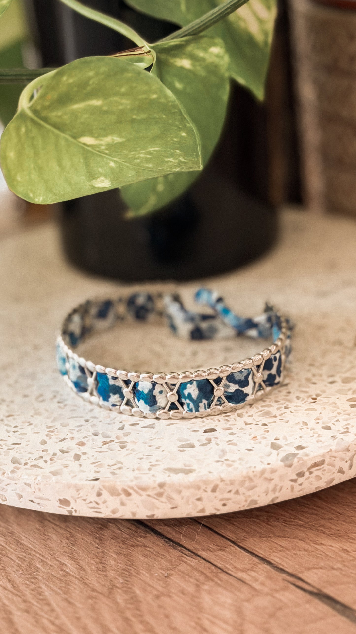 Bracelet jonc en acier inoxydable et tissu upcyclé argenté motif fleurs bleu marine, posé sur un plateau en terrazzo
