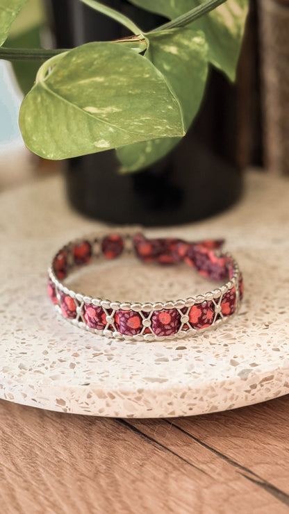 Bracelet jonc en acier inoxydable et tissu upcyclé argenté motif fleurs bordeaux, posé sur un plateau en terrazzo