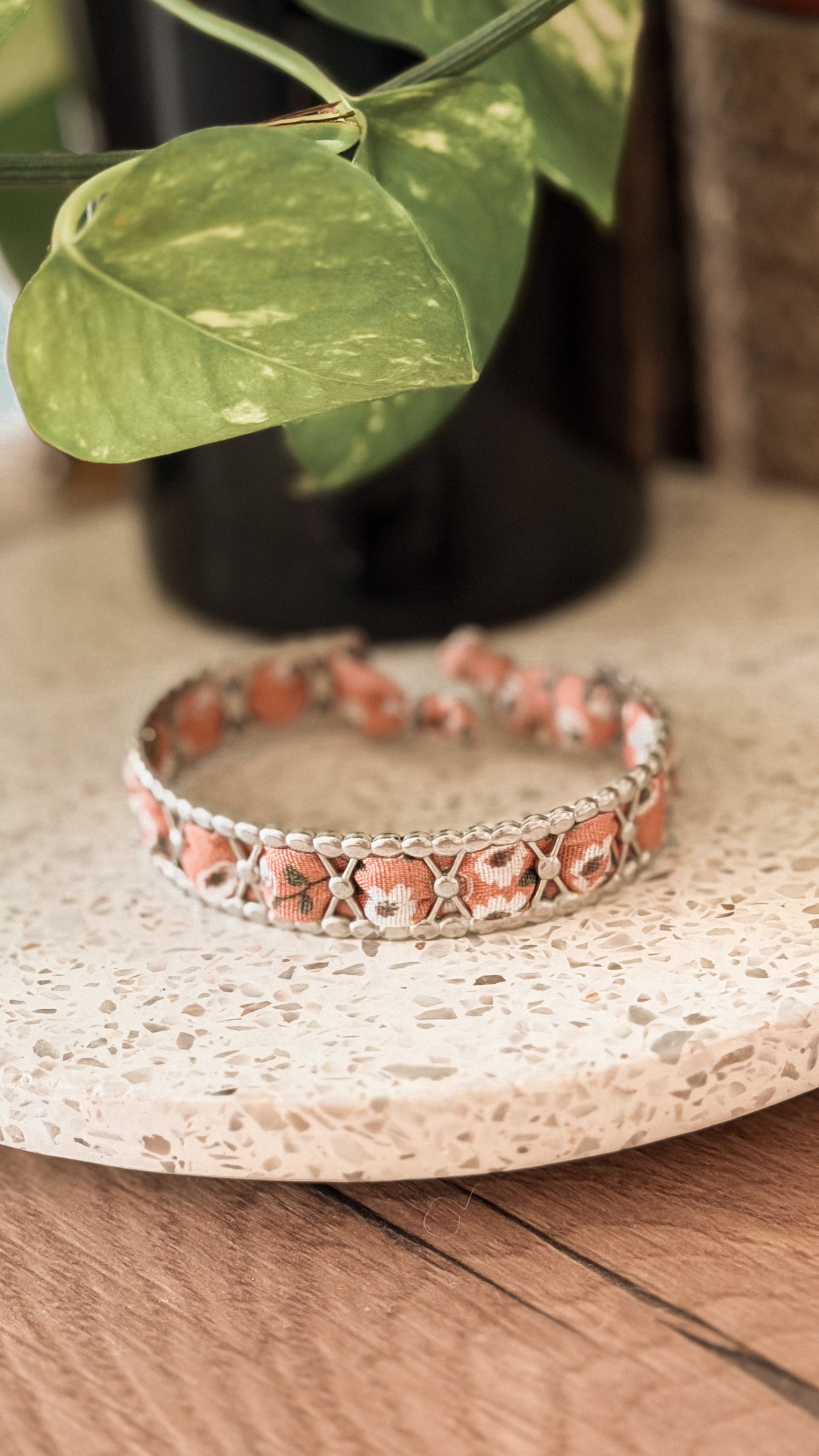 Bracelet jonc en acier inoxydable et tissu upcyclé argenté motif fleurs corail, posé sur un plateau en terrazzo