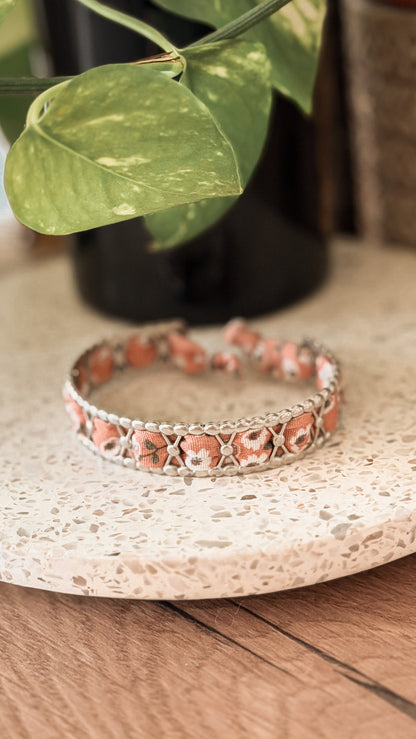 Bracelet jonc en acier inoxydable et tissu upcyclé argenté motif fleurs corail, posé sur un plateau en terrazzo