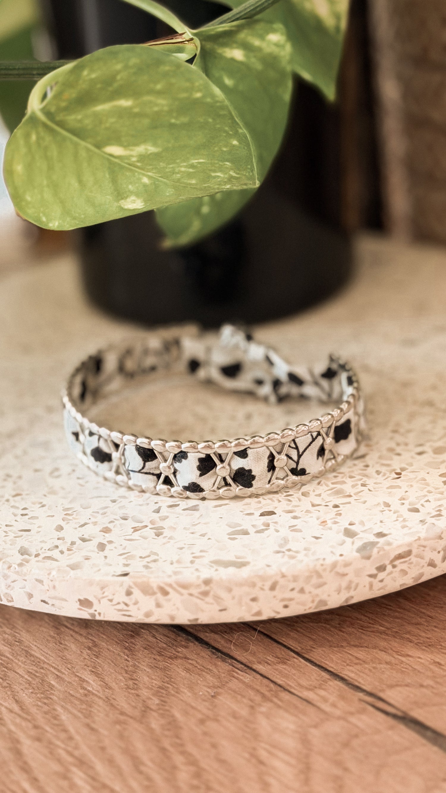 Bracelet jonc en acier inoxydable et tissu upcyclé argenté motif fleurs noir et blanc, posé sur un plateau en terrazzo
