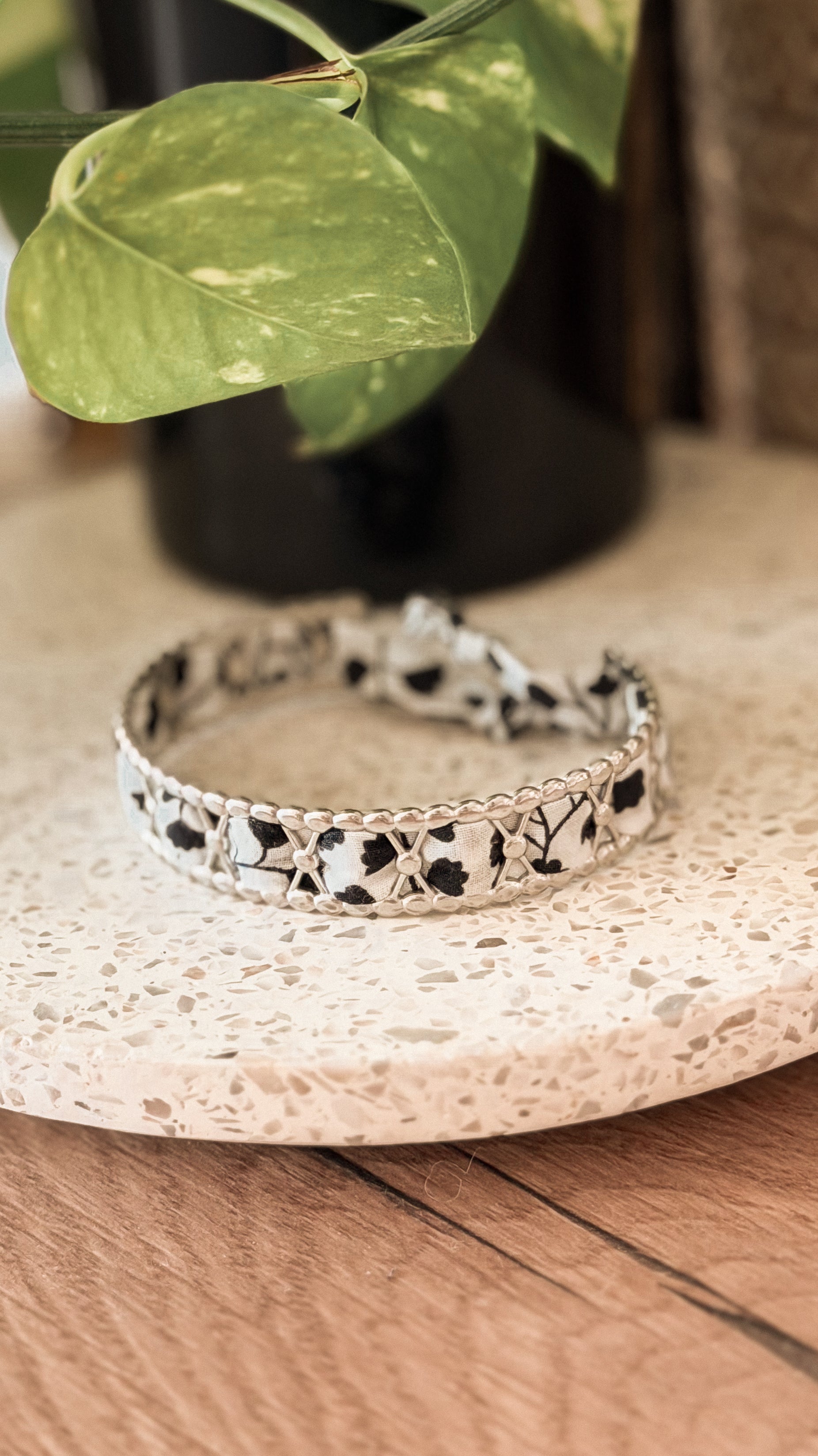 Bracelet jonc en acier inoxydable et tissu upcyclé argenté motif fleurs noir et blanc, posé sur un plateau en terrazzo