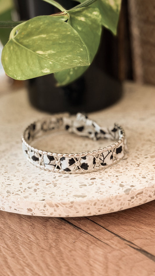 Bracelet jonc en acier inoxydable et tissu upcyclé argenté motif fleurs noir et blanc, posé sur un plateau en terrazzo