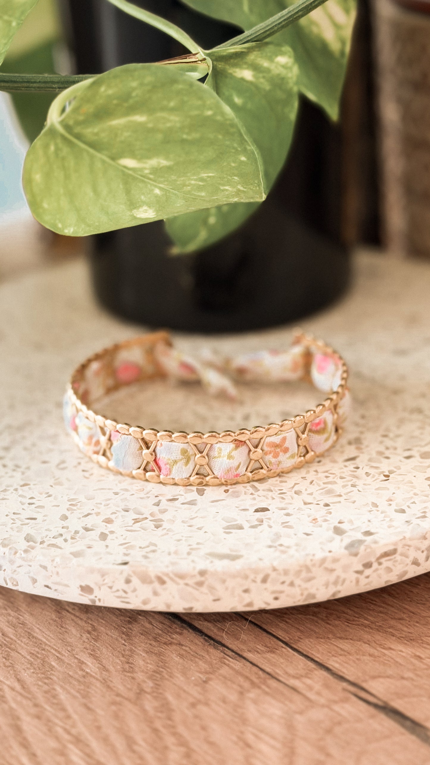 Bracelet jonc en acier inoxydable et tissu upcyclé motif fleurs roses pastel, posé sur un plateau en terrazzo