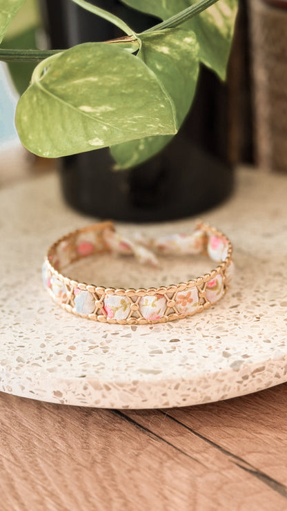 Bracelet jonc en acier inoxydable et tissu upcyclé motif fleurs roses pastel, posé sur un plateau en terrazzo