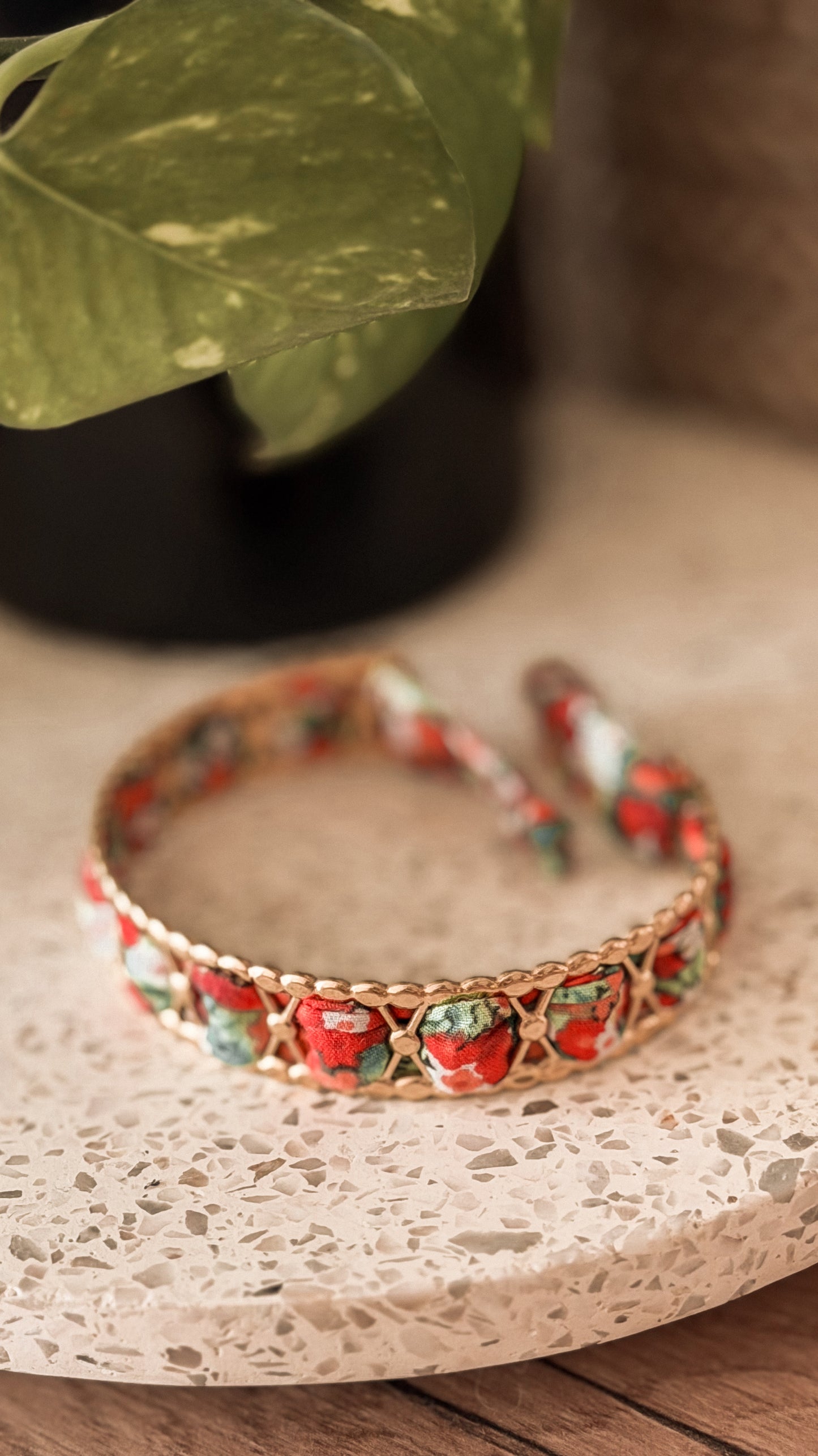 Bracelet jonc en acier inoxydable et tissu upcyclé motif fleurs rouges et vertes, posé sur un plateau en terrazzo