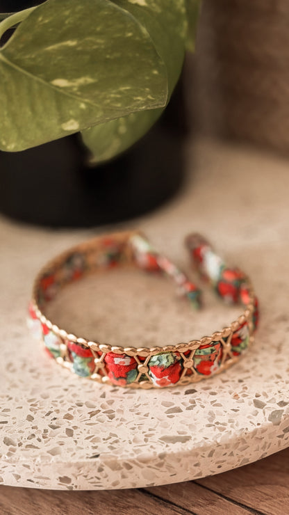 Bracelet jonc en acier inoxydable et tissu upcyclé motif fleurs rouges et vertes, posé sur un plateau en terrazzo