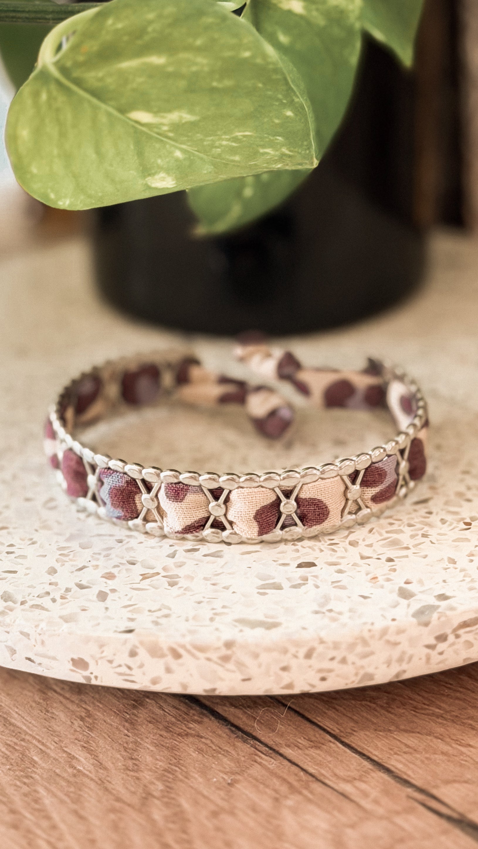 Bracelet jonc en acier inoxydable et tissu upcyclé argenté motif léopard bordeaux et beige, posé sur un plateau en terrazzo