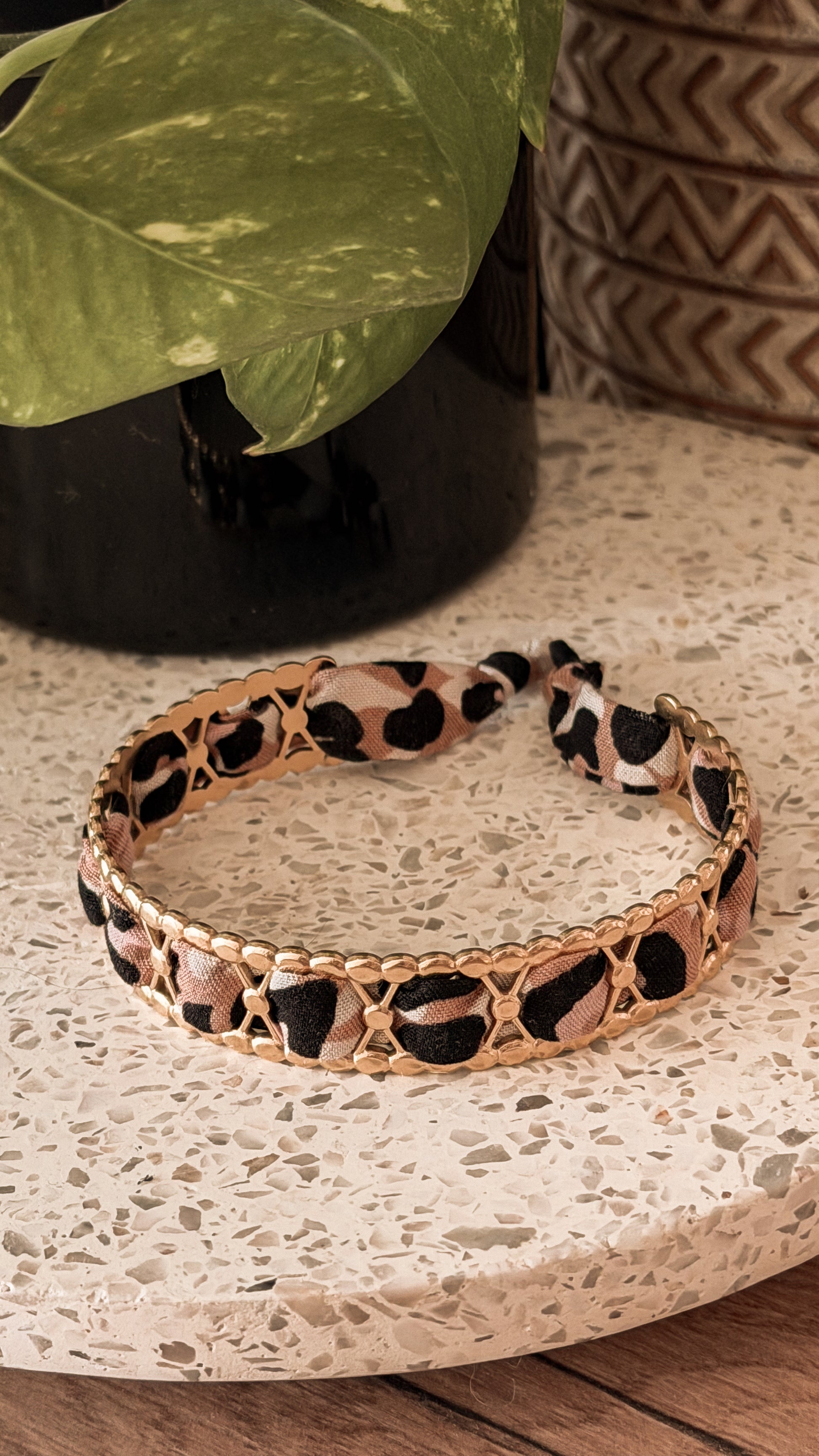 Bracelet jonc en acier inoxydable et tissu upcyclé motif léopard noir et beige, posé sur un plateau en terrazzo