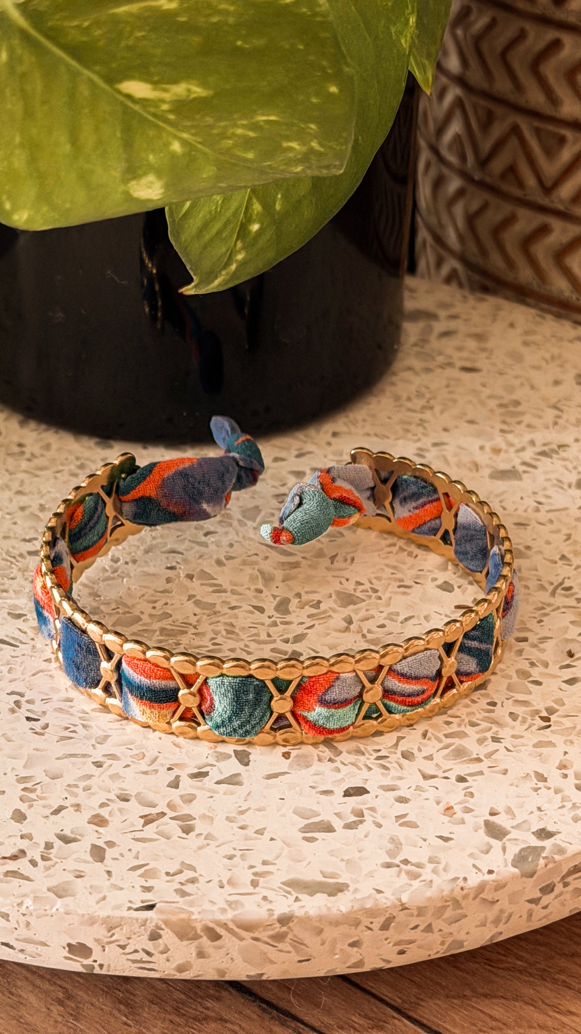 Bracelet jonc en acier inoxydable et tissu upcyclé motif abstrait bleu et orange, posé sur un plateau en terrazzo