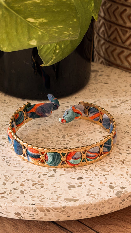 Bracelet jonc en acier inoxydable et tissu upcyclé motif abstrait bleu et orange, posé sur un plateau en terrazzo