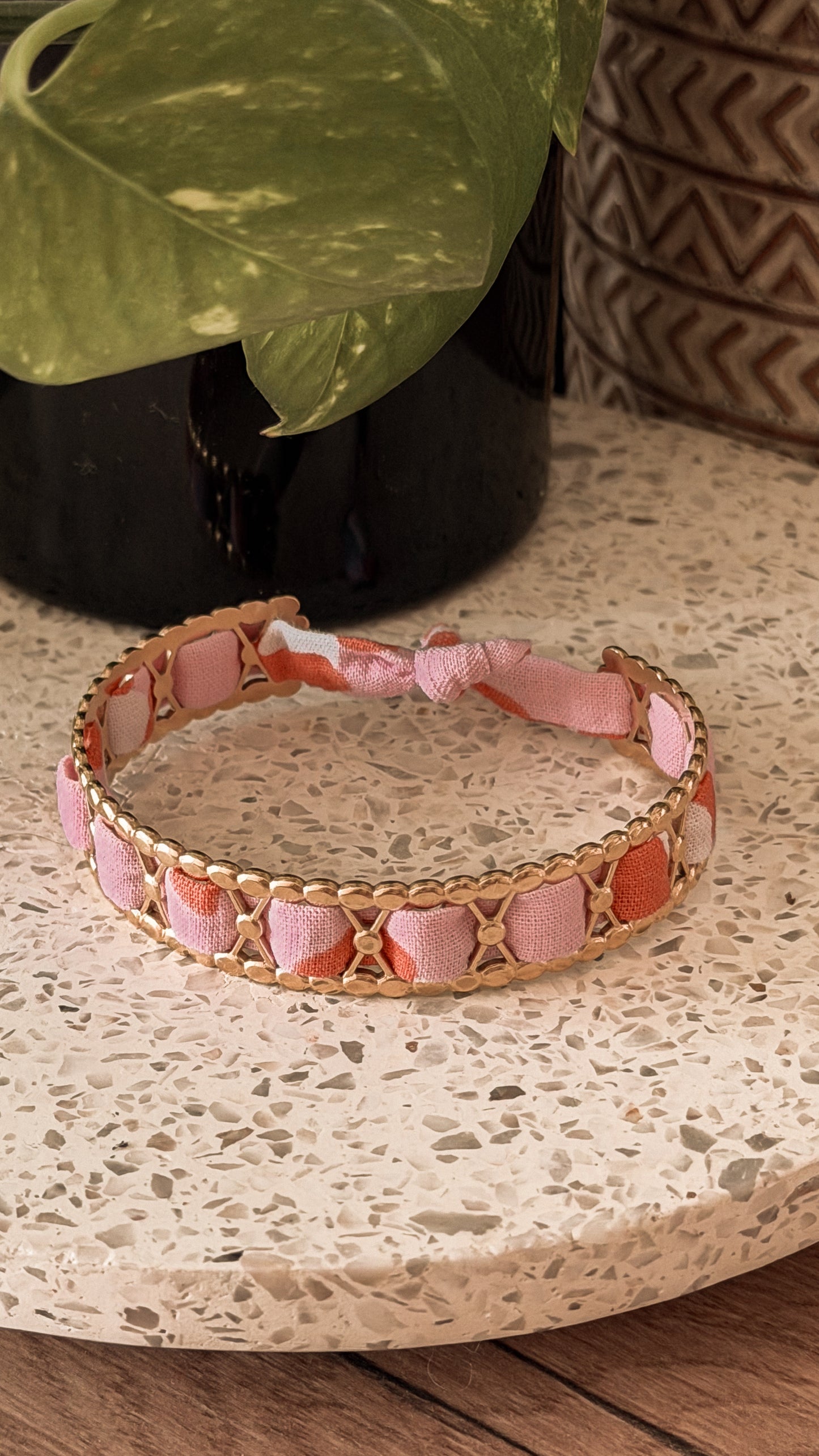 Bracelet jonc en acier inoxydable et tissu upcyclé motif damier rose et corail, posé sur un plateau en terrazzo